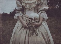 an old fashion photo of a woman holding a skull in her hands and wearing a long dress