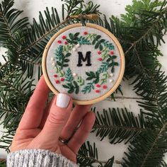 someone is holding up a cross stitch ornament with the letter m on it