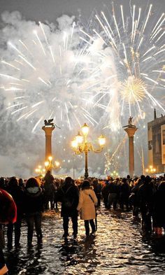 people are standing in the water watching fireworks