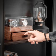 a man is pointing at two watches in a glass display case on a wooden shelf