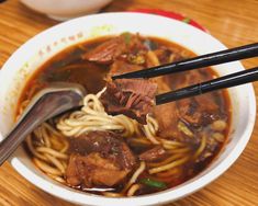 two chopsticks holding noodles in a bowl with beef and meat on it, ready to be eaten