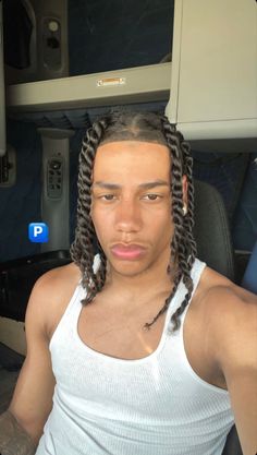 a man with dreadlocks sitting in an airplane looking at the camera while wearing a white tank top