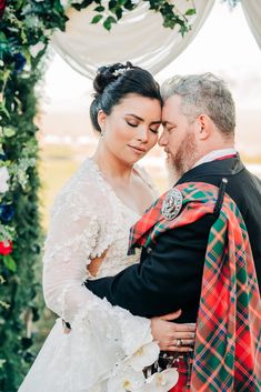 a bride and groom embracing each other in front of an arch decorated with greenery