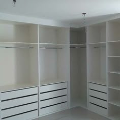 an empty walk in closet with white shelves and drawers