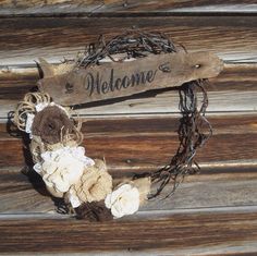 a welcome sign is hanging on the side of a wooden wall with flowers and burlap