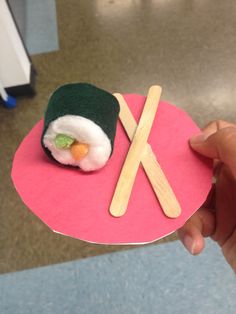 a hand holding a piece of paper with sushi on it and chopsticks sticking out of it