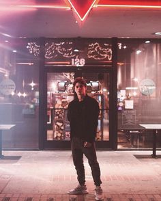 a man standing in front of a building with a neon sign on it's side