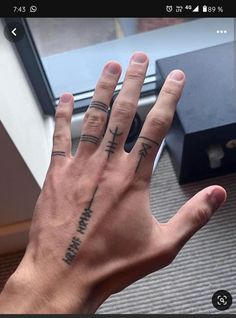 a person's hand with two small tattoos on it, and the other hand is in front of a window