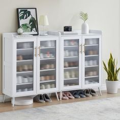 a white cabinet with several pairs of shoes on it and a potted plant next to it