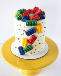 a lego cake with white frosting and multicolored blocks on the top, sitting on a yellow plate