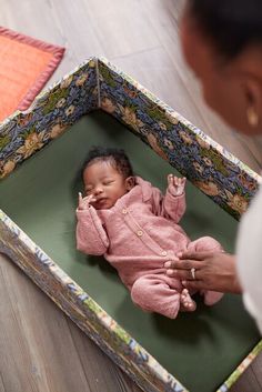 a baby is laying in a box on the floor and being held by a woman