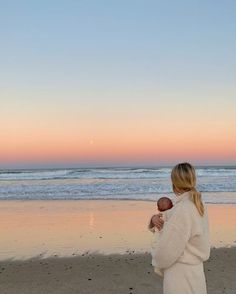 a woman standing on top of a beach holding a baby