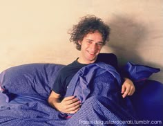 a man laying in bed covered with a blue comforter and smiling at the camera