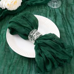 a white plate topped with green napkins next to a glass and flower on a table