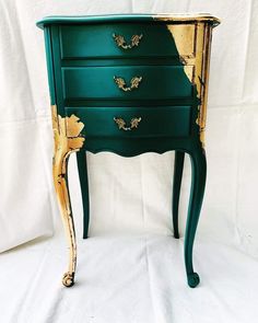 a green and gold painted chest of drawers on a white sheeted background, with one drawer open