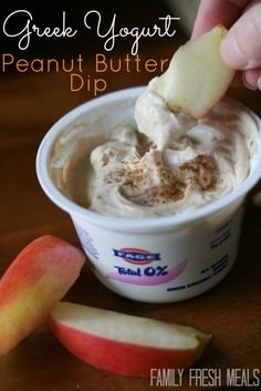 a person dipping an apple into a cup of peanut butter dip with cinnamon on top