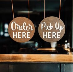 two wooden signs that say order pick up here and pick up now hanging from strings