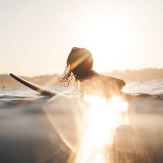 a person riding on top of a surfboard in the middle of the ocean at sunset