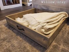 a wooden box with blankets in it sitting on the floor next to a bed and pillows