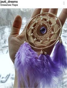 a person holding up a small dream catcher in their hand with purple feathers on it