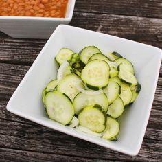 sliced cucumbers in a square white bowl next to a dish of chili sauce