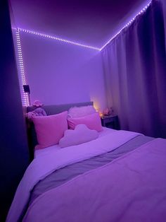 a bed with pink and purple pillows in a room that has lights on the walls