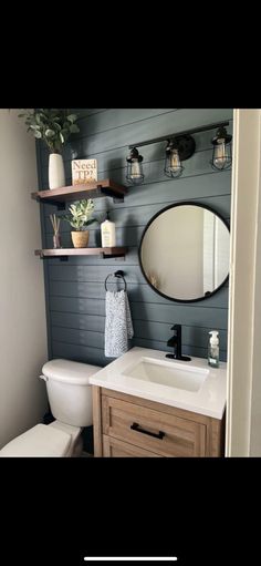 a white toilet sitting next to a bathroom sink under a round mirror on top of a wooden cabinet