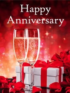 two glasses of champagne with red roses and gift boxes in the background, happy anniversary card