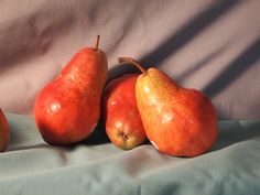 three pears and two oranges on a blue cloth background with shadows from the fabric