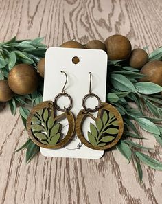 the wooden earrings are decorated with green leaves and brown wood circles, on top of a table