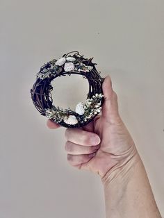 a hand holding a wreath with flowers and leaves on the inside, in front of a white wall