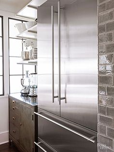 a stainless steel refrigerator in a kitchen next to a brick wall and wooden flooring