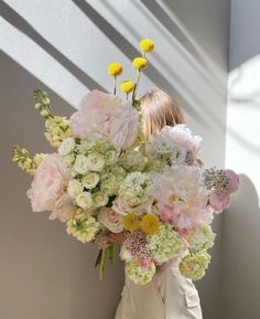 a woman holding a large bouquet of flowers in her hands while standing next to a wall