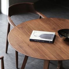 a wooden table with a book on it and two chairs around it in front of a window