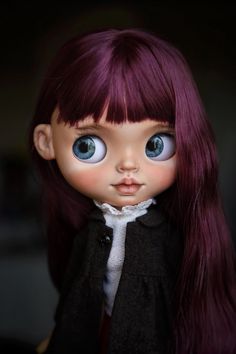 a close up of a doll with long hair and blue eyes wearing a black jacket