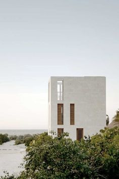 a white building sitting on top of a lush green hillside next to the ocean and trees