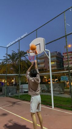 a man is playing basketball on an outdoor court at night with his hands up in the air