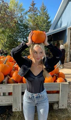 a woman standing in front of a pile of pumpkins with her hands on her head