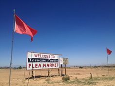 a welcome sign and two flags in the middle of nowhere, with a blue sky behind it