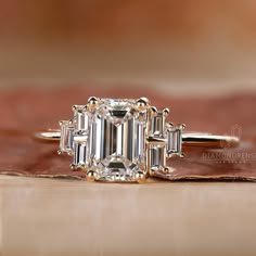 an emerald - cut diamond ring with baguettes on top sits on a piece of wood