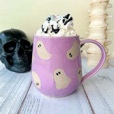 a purple coffee mug with marshmallows and black skulls on the side next to it