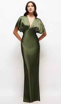 a woman in a long green dress standing with her hands on her hips and looking off to the side