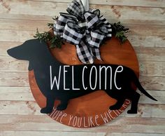 a welcome sign hanging on the side of a wooden wall with a black and white dachshund