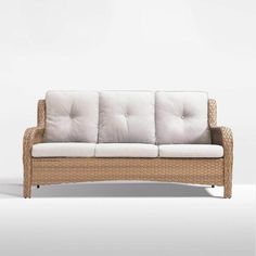 a wicker couch sitting on top of a white floor next to an empty wall