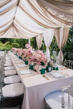 a long table set up with white linens and pink flowers on it for an outdoor wedding reception