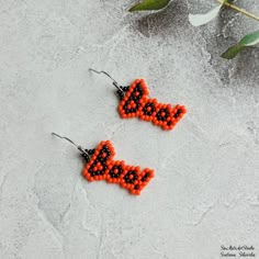 two orange and black beaded earrings sitting on top of a white surface next to a plant