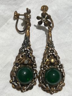 Vintage from 1940s. Beautiful ,brass plated, I believe Jade, dangle, drop, hanging, long, earrings. Has pretty floral with pearl colors on top. Great victorian style earrings. Colors are bronze, pearl, gold,  green. Look like also has swarovski gems that are little dim from age. **The green gem looks like jade, or jade glass, green glass. I DO NOT KNOW  for sure if its jade. Sold as is.   In good condition. Brass has worn off in places, white patina,  Also has patina from old age. Sold as is. ** Antique Green Jewelry For Evening, Antique Style Drop Earrings With Antique Finish, Ornate Green Jewelry For Evening, Victorian Drop Earrings For Vintage Events, Antique Metal Earrings For Evening, Antique Drop Earrings For Vintage Collection, Vintage Dangle Earrings For Evening, Green Costume Jewelry Earrings For Wedding, Vintage Dangle Jewelry