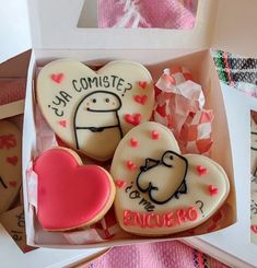 four decorated cookies in a box with writing on the top and hearts at the bottom