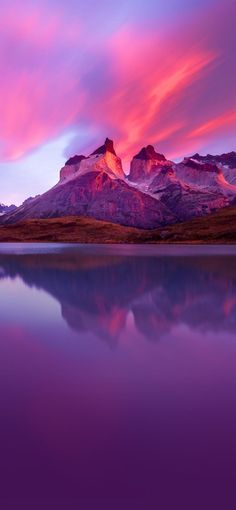 the mountains are covered in pink clouds and reflecting water at sunset or sunrise, as seen from an alpine lake