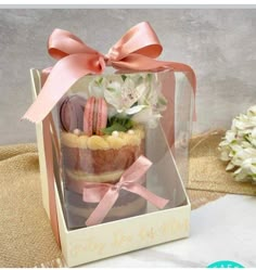 a small cake in a box with pink ribbon and flowers on the top, sitting on a table